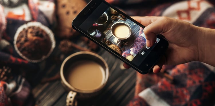 Someone taking a picture of a cup of coffee with their cellphone. Someone taking a picture of a cup of coffee with their cellphone.