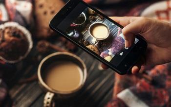 Someone taking a picture of a cup of coffee with their cellphone.