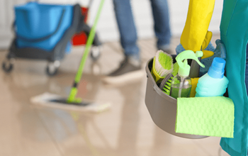 Two cleaning employees, mopping and carrying a cleaning caddy.