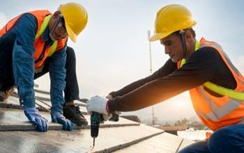 Two people in helmets working on a roof.