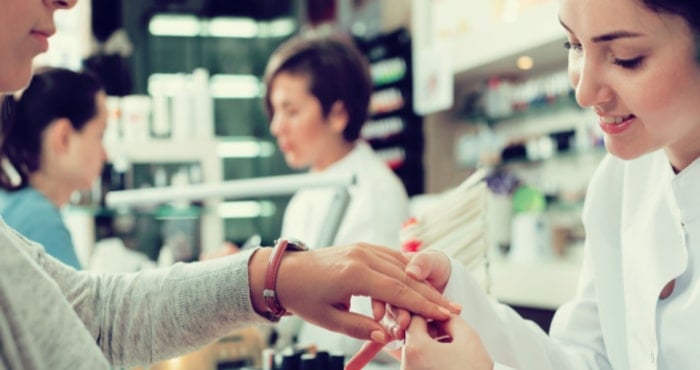 A nail salon technician works on a customer's hand