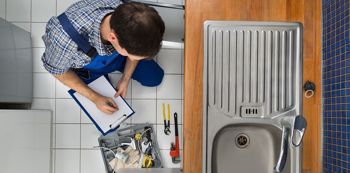 Plumber inspecting kitchen sink with tools and writing notes. Plumber inspecting kitchen sink with tools and writing notes.