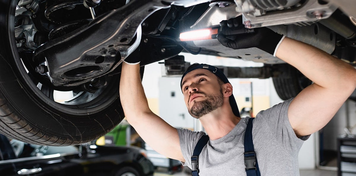 Mechanic inspecting car underside with work light. Mechanic inspecting car underside with work light.