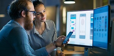 Designers reviewing mobile app on monitors and smartphone.