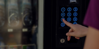 Person pushing a button on the keypad of a soda machine.
