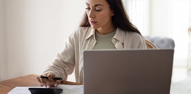 Woman reviewing financial documents on a laptop with a calculator.