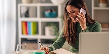 Person on the phone taking notes in a home office.
