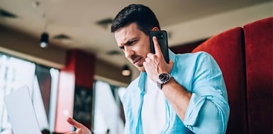 Person talking on the phone while using a laptop computer.