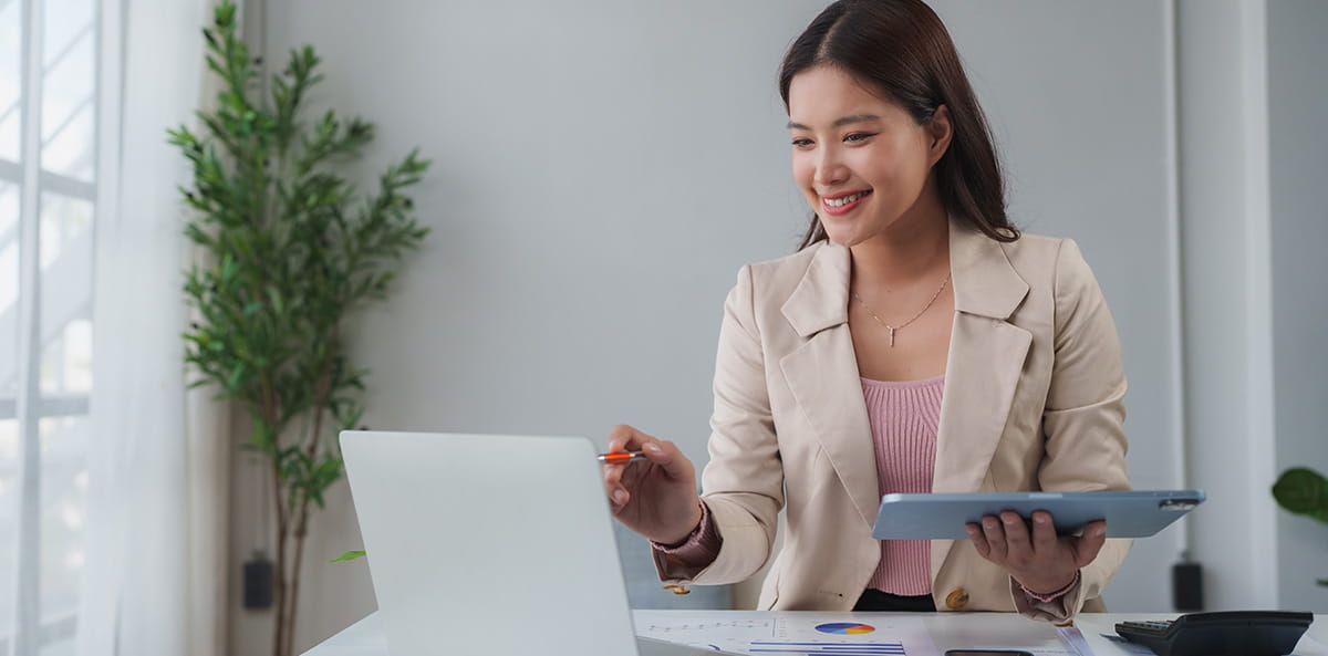 A businesswoman working on laptop and tablet at desk.