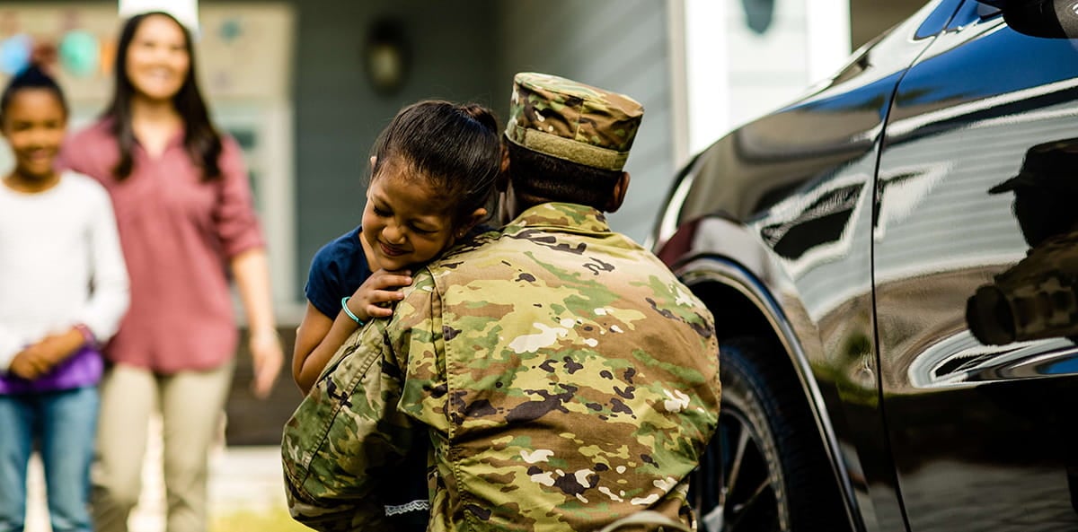 A military father embracing his daughter during a homecoming with his family watching in the background. A military father embracing his daughter during a homecoming with his family watching in the background.