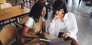 Small business owner discussing content on a laptop at a café workspace.
