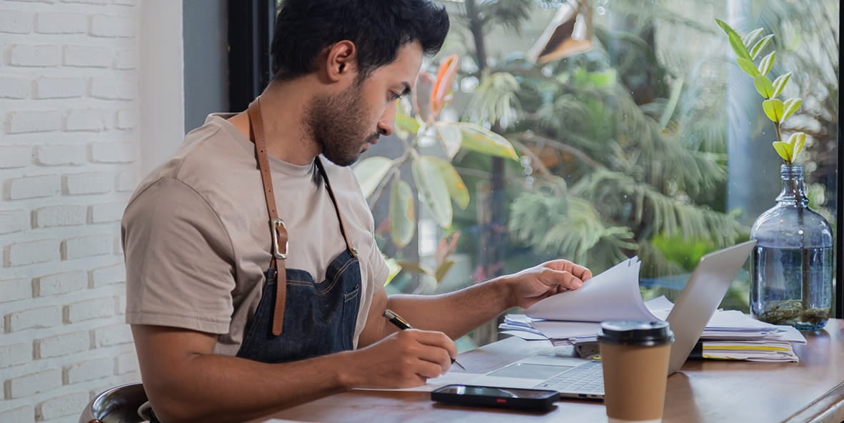 Business owner working on tax returns at a table with a laptop. Business owner working on tax returns at a table with a laptop.