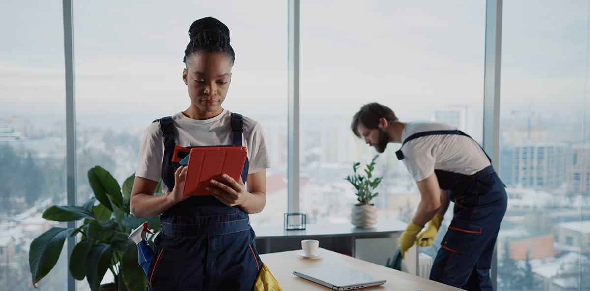 Office cleaners using a tablet while cleaning a workspace. Office cleaners using a tablet while cleaning a workspace.