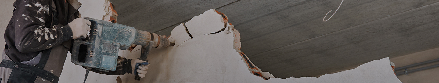 A contractor uses a demolition hammer to take apart a wall.