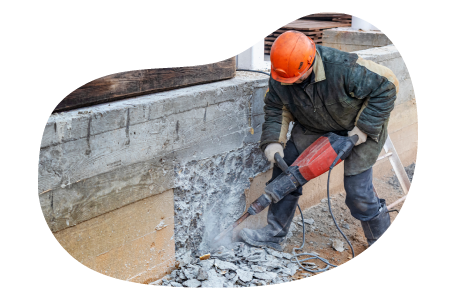 A demolition contractor works on a foundation with a jackhammer.