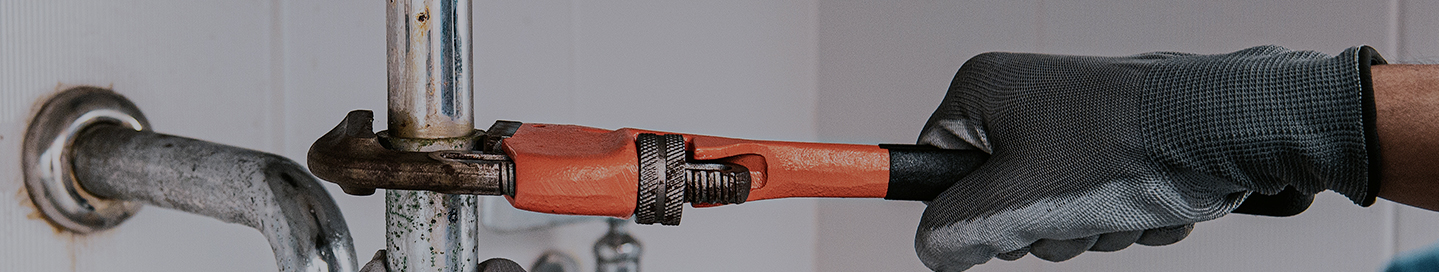 A drain cleaning contractor uses a wrench on a clogged pipe.