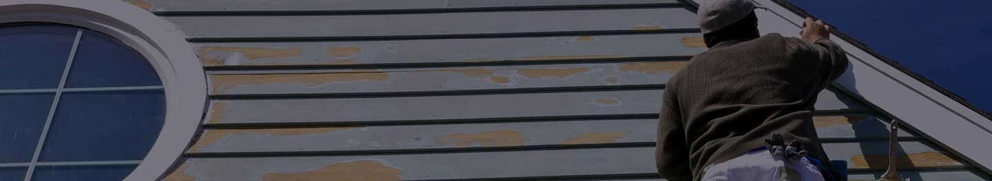 Painter on a ladder painting the exterior of a house.