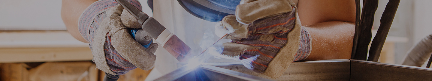 A welder in helmet and gloves working on a construction project.