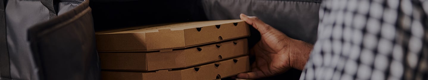 A delivery driver stores pizzas in their insulated delivery bag. A delivery driver stores pizzas in their insulated delivery bag.