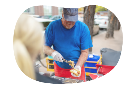 Employee assembling hot dog at their hot dog cart. Employee assembling hot dog at their hot dog cart.