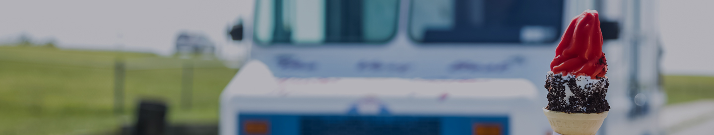 An ice cream cone held up in front of an ice cream truck.