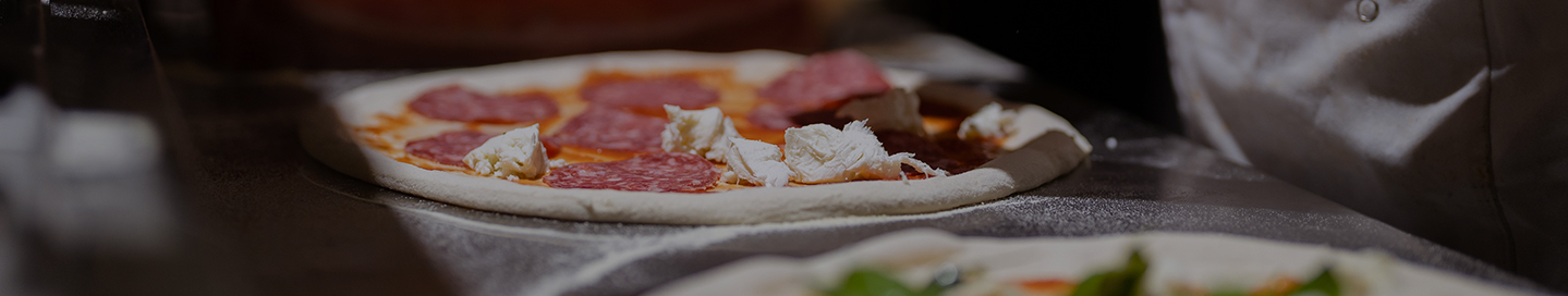 An employee putting cheese and pepperoni on a pizza.