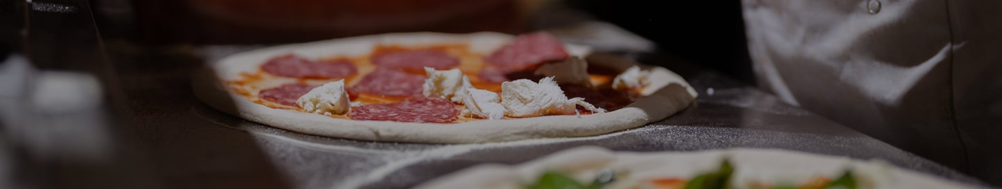 An employee putting cheese and pepperoni on a pizza. An employee putting cheese and pepperoni on a pizza.