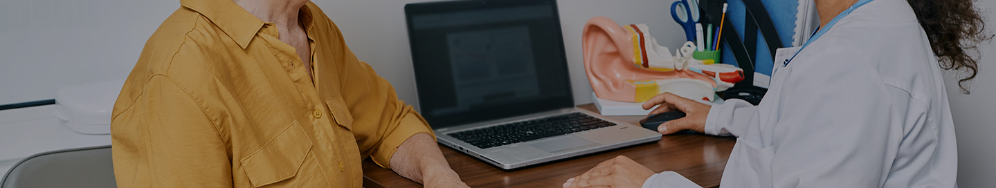 An audiologist speaks with a patient next to a model of an ear.