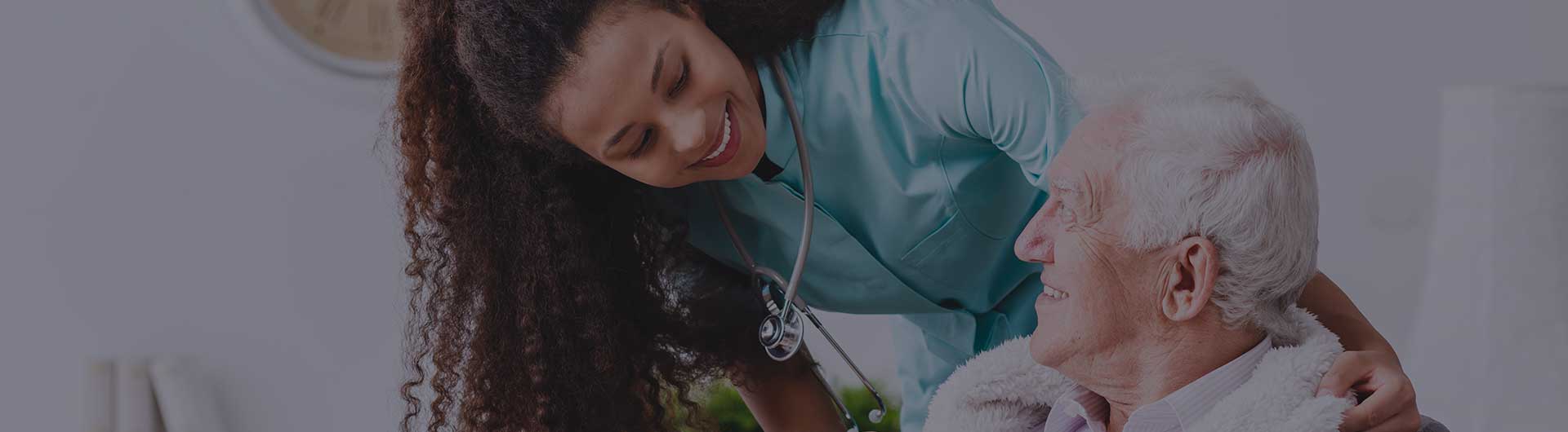 A smiling nurse with a stethoscope covering an elderly person with a blanket in a nursing home.