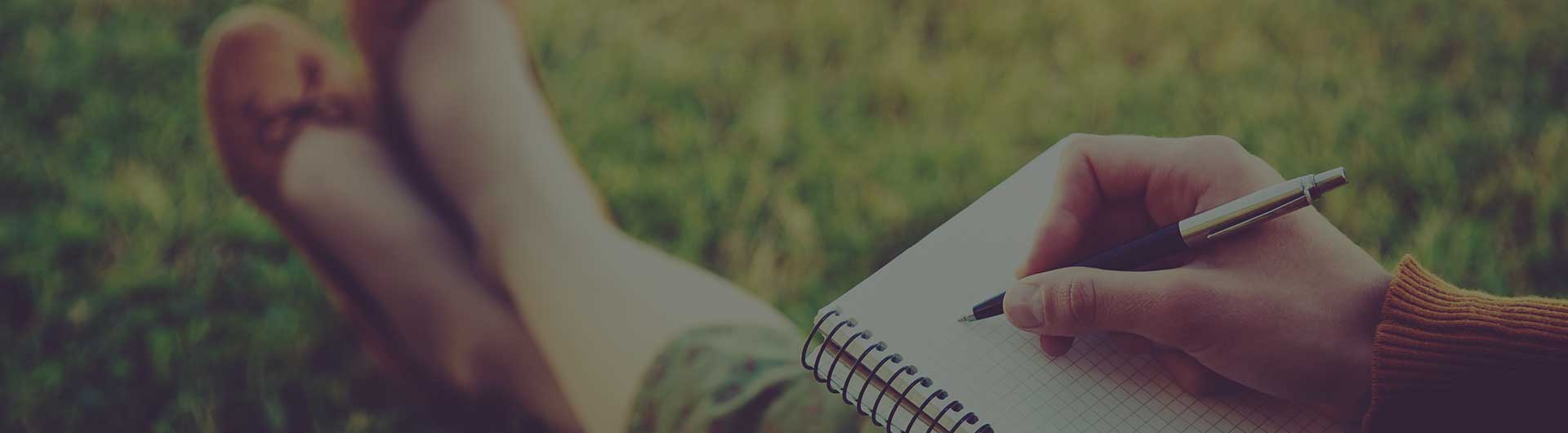 Female writer sitting in park writing on a pad of paper.