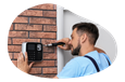 A contractor installs an alarm keypad at the front door of a home.