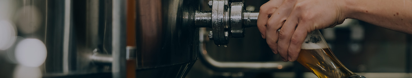 A brewer pulls a sample of beer from a fermenter's tap.