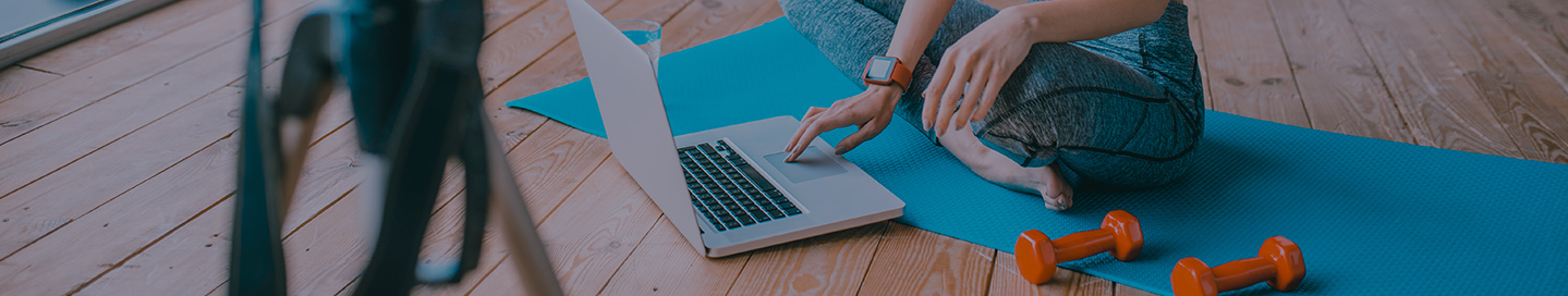 A blogger sitting on a yoga mat and typing on a laptop.