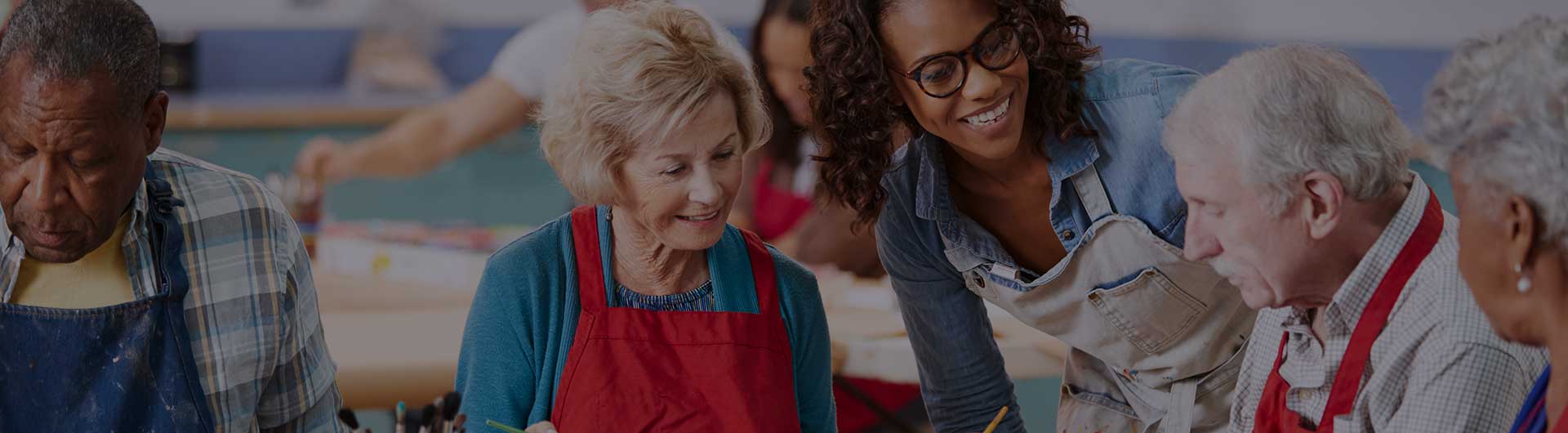 Group of retired seniors attending art class in community centre with teacher.