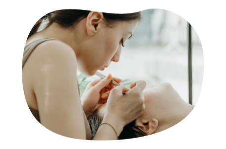 A brow and lash technician works on a client with tweezers.