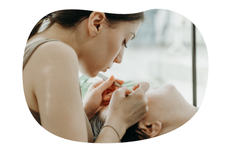 A brow and lash technician works on a client with tweezers. A brow and lash technician works on a client with tweezers.