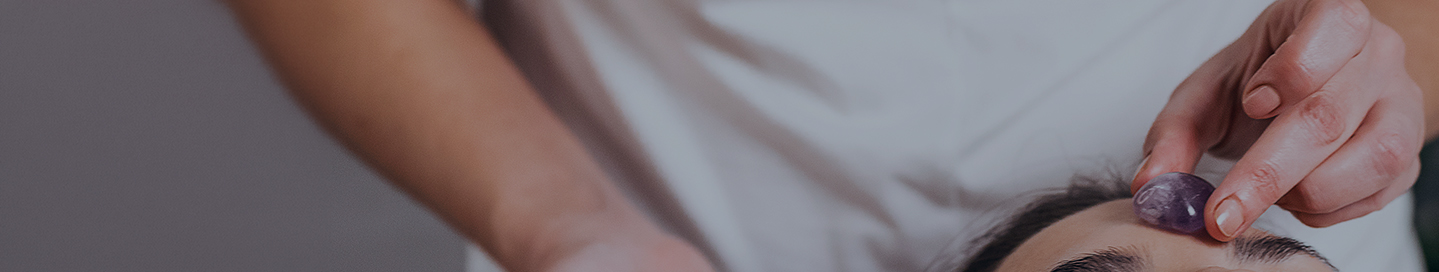 A Reiki practitioner places a healing stone on a client's forehead.