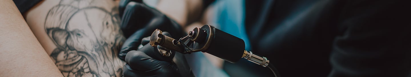 A tattoo artist creates a design on a client's arm. A tattoo artist creates a design on a client's arm.