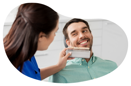 A dental assistant shows a client a tooth shade guide as part of a teeth whitening procedure.