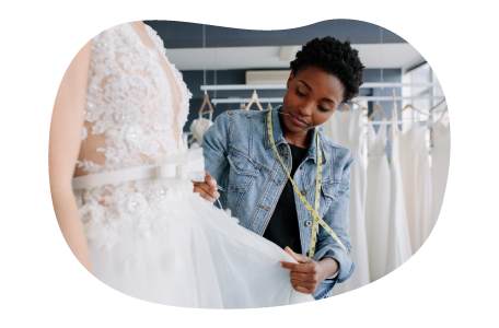 Bridal shop employee measuring a client wearing a wedding dress.