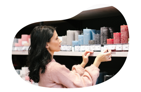 Candle shop employee placing pricing on a store shelf holding candles.
