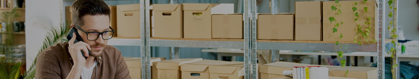 An eBay seller on the phone in front of shelves of boxes. An eBay seller on the phone in front of shelves of boxes.