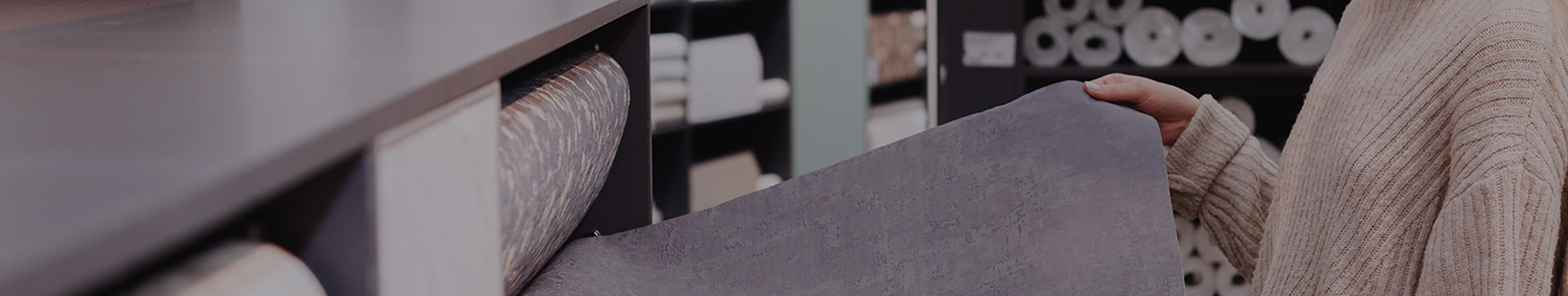 A business owner examines a roll of wallpaper in their paint and wallpaper store.