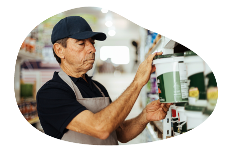 A business owner examines a can of paint in their paint and wallpaper store.