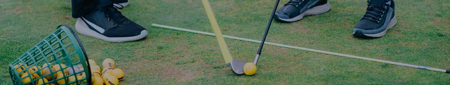 A golf instructor teaches a student using an alignment stick.