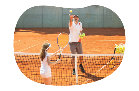 A tennis instructor tosses a ball to a student. A tennis instructor tosses a ball to a student.
