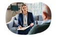 Social worker sitting on a couch speaking with a client at their home.