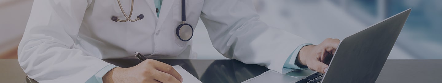 Medical professional working with a laptop and a stack of papers.