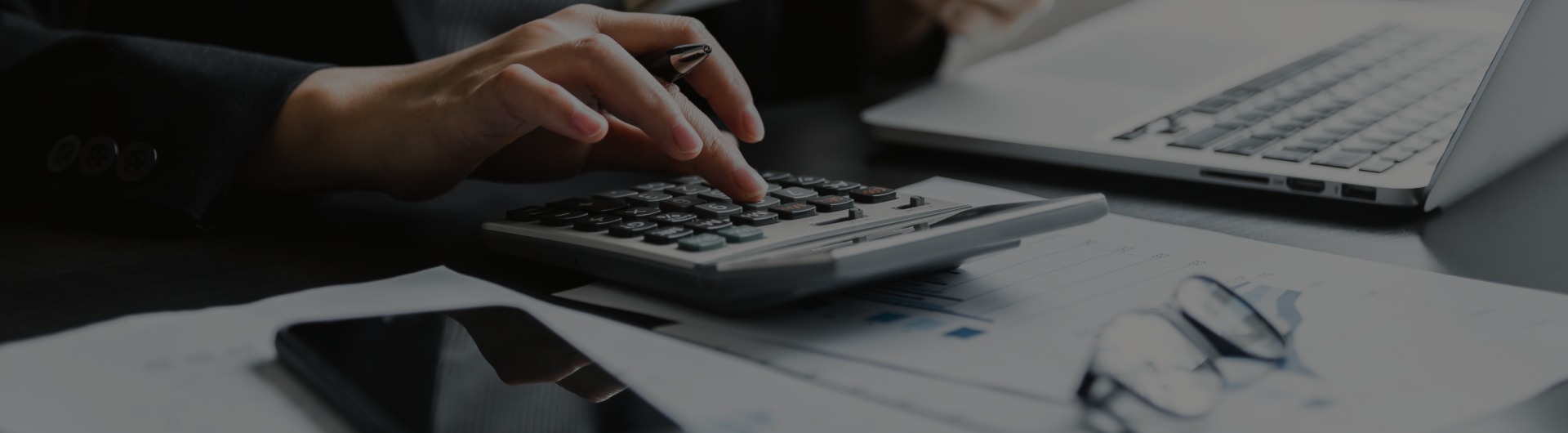 Person using a calculator at a desk with financial documents and a laptop.