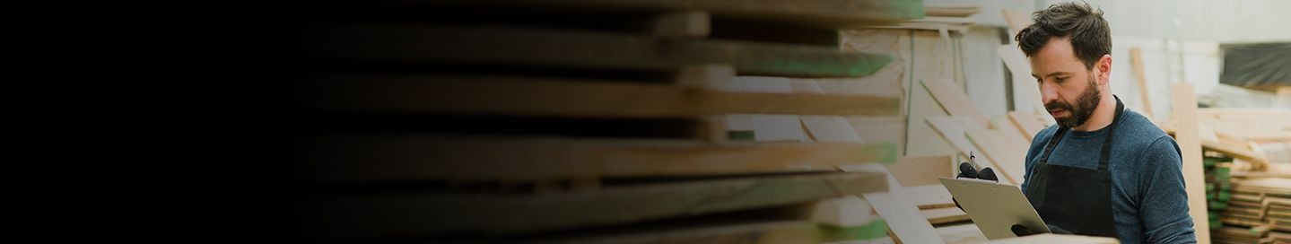 Business owner in woodshop consulting clipboard.